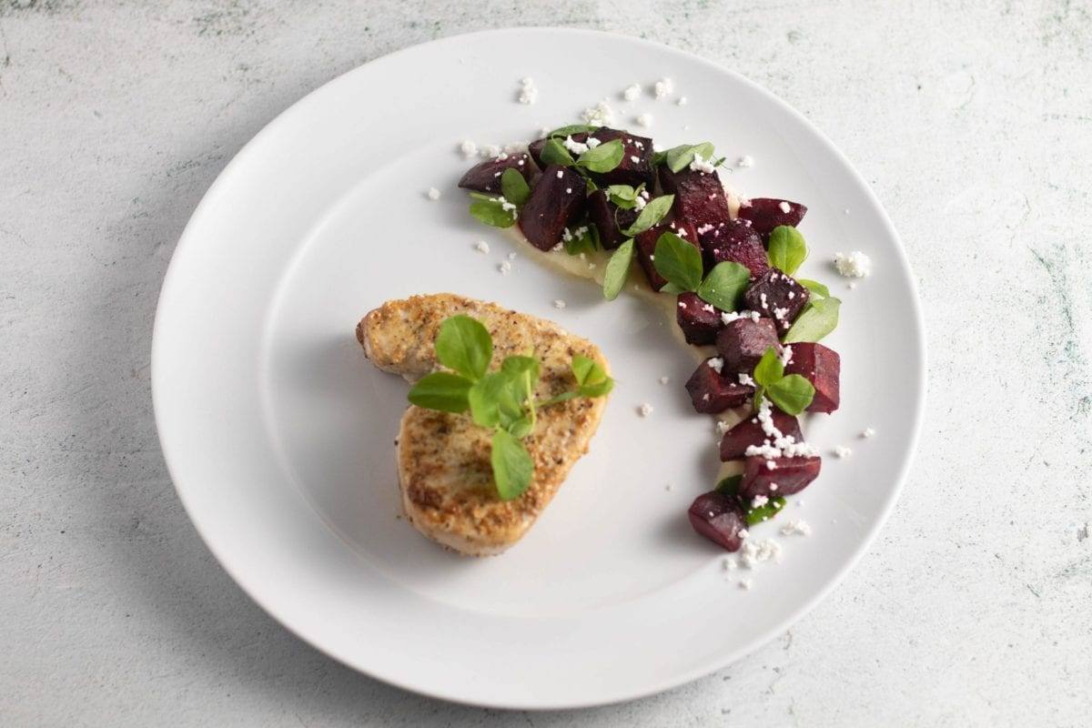 Swordfish Roasted Beet Parsnip Puree served on a white plate, sprinkled with micro greens and goat cheese