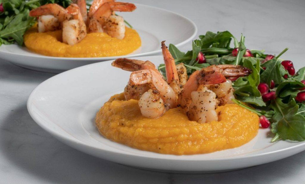 Roasted Butternut Squash Puree with Shrimp on two white plates sitting on top of a marble countertop