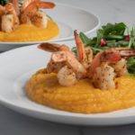 Roasted Butternut Squash Puree with Shrimp on two white plates sitting on top of a marble countertop