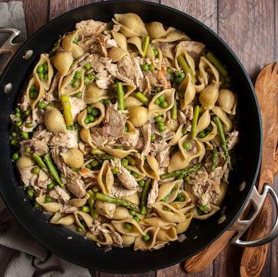 Creamy Chicken Pastas with Peas and Asparagus in a large black pan with a gray napkin next to it and a wooden serving spoon Freezer friendly