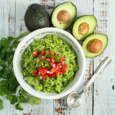 Basic Guacamole topped with tomatoes and surrounded by cut avocados and a serving spoon