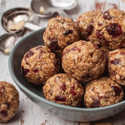 Cranberry Oatmeal Bliss Balls in a blue bowl with heat shaped metal measuring spoons next to them. 