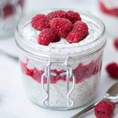 Raspberry Chia Seed Pudding in glass canning jars, topped with fresh raspberries, small metal serving spoon next to it