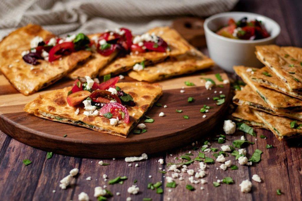 Greek Breakfast Quesadilla w/Spinach & Mushroom Meal Planning Meal Prep Counting Macros on a cutting board sprinkled with feta, tomatoes, and olives.