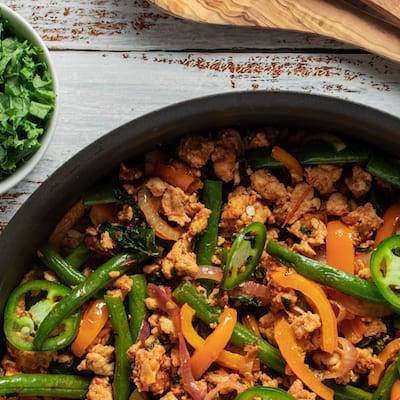 Turkey Kale and Green Bean One Pot Meal served in a black skillet with a bowl of chopped kale and a wooden spoon