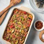 Zucchini & Ground Beef Orzo Casserole, In a cream and blue casserole dish, with red pepper flake. Great for meal prep, freezer friendly, and can be easily adjusted to fit your goals if your counting macros, add this recipe to your meal plan today.