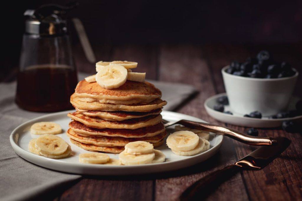 Easy, Healthy High Protein Banana Pancakes, served on a white plate with bananas on top and drizzled with syrup
