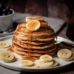 Easy, Healthy High Protein Banana Pancakes, served on a white plate with bananas on top and drizzled with syrup