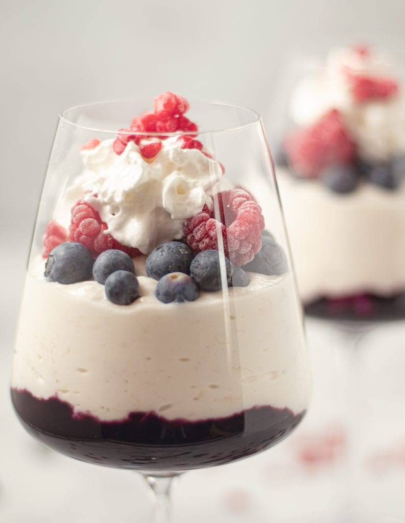 Healthy Blueberry Compote & Banana Yogurt Parfait served in a wine glass topped with frozen raspberries