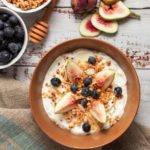 Fig Yogurt Parfait severs in a brown bowl with blueberries on top with granola and honey.