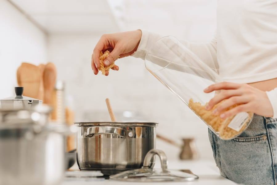 Women wear white shirt and jeans Reheating Meal Prepped Food on a stove in a pot