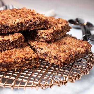 Oat and Date Bars, stacked on top of each other on a metal drying wrack with heart shaped measuring spoons next to them.